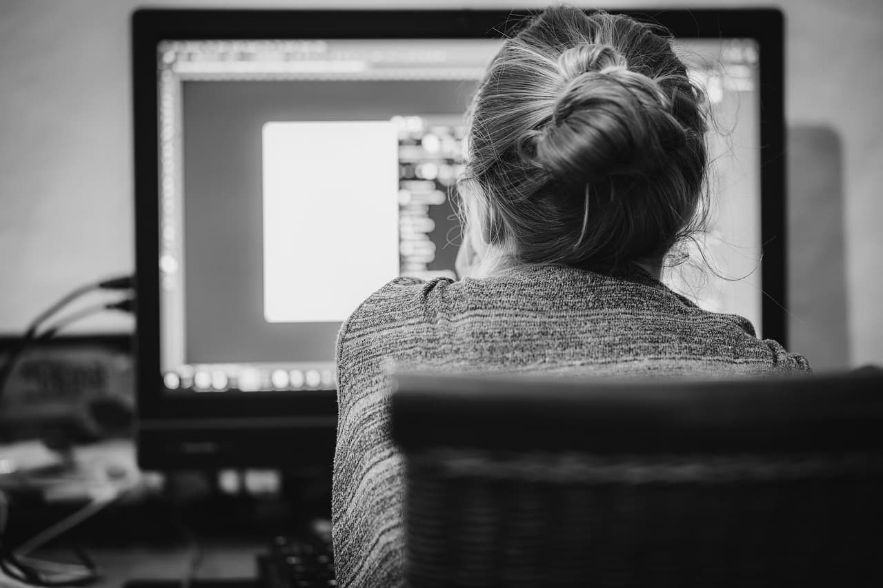 Uma pessoa a trabalhar em frente ao ecrã de um computador, a analisar um documento num monitor de secretária